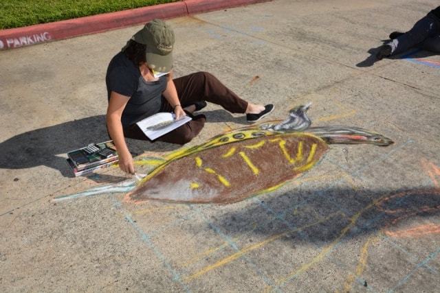 Chalk artist seated on the pavement creating a detailed sea turtle mural at CreekFest Houston