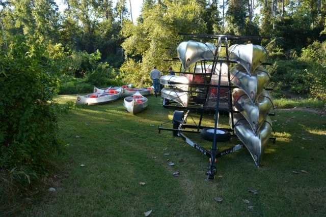Canoes and kayaks stacked on a trailer and laid on the grass at the Cypress Creek launch area at CreekFest