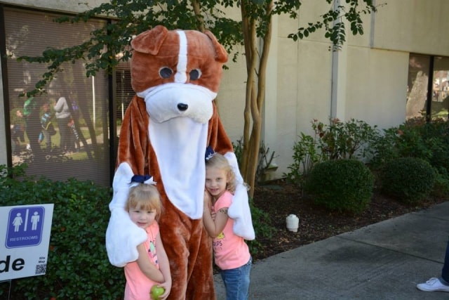 Two young girls hugging a dog mascot at CreekFest Houston