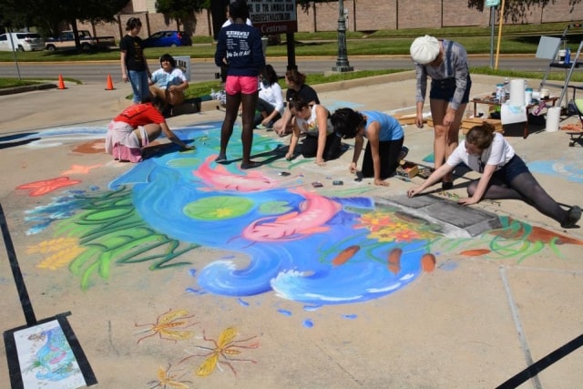 Team of chalk artists working together on a large mermaid mural at CreekFest