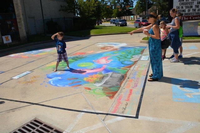 Family admiring a large colorful chalk mural on the pavement at CreekFest