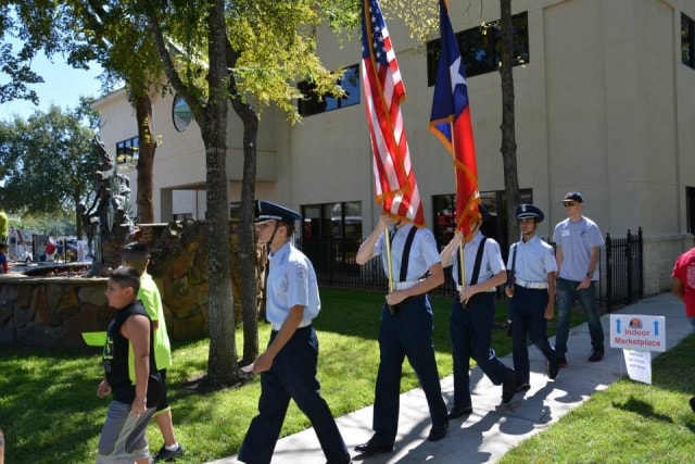 ROTC color guard marching with American and Texas flags past the Indoor Marketplace sign at CreekFest