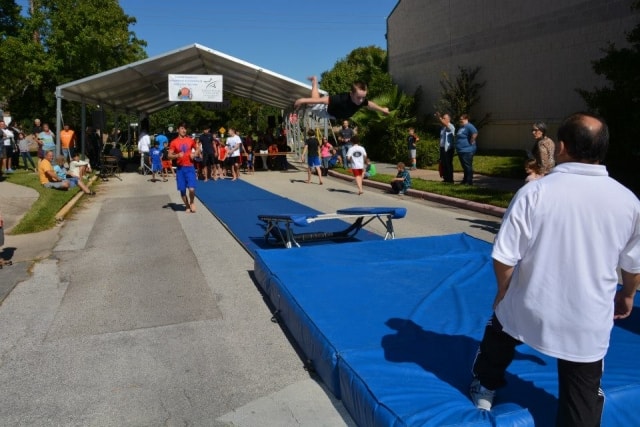 Gymnast performing a vault over a springboard onto a blue crash mat at CreekFest Houston