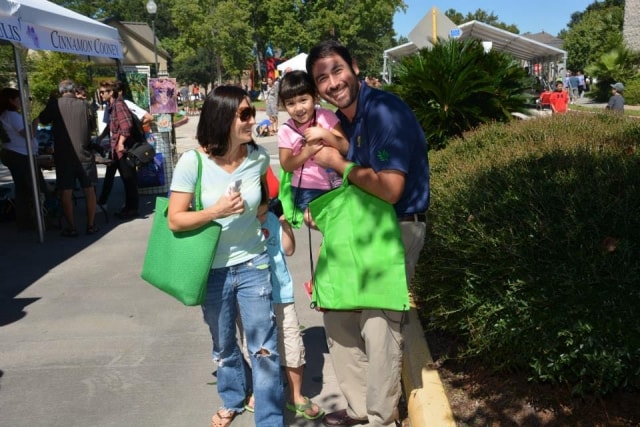 Family of three smiling together among vendor booths at CreekFest Houston