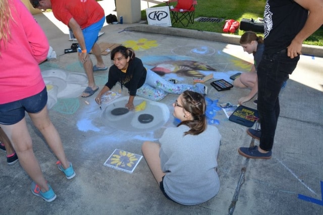 Students creating a chalk art mural on the pavement at CreekFest Houston