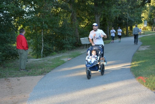 Father jogging with a baby stroller on the Cypress Creek greenway trail at CreekFest