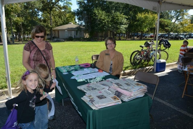 Family checking in at a green-draped information table under a canopy at CreekFest Houston