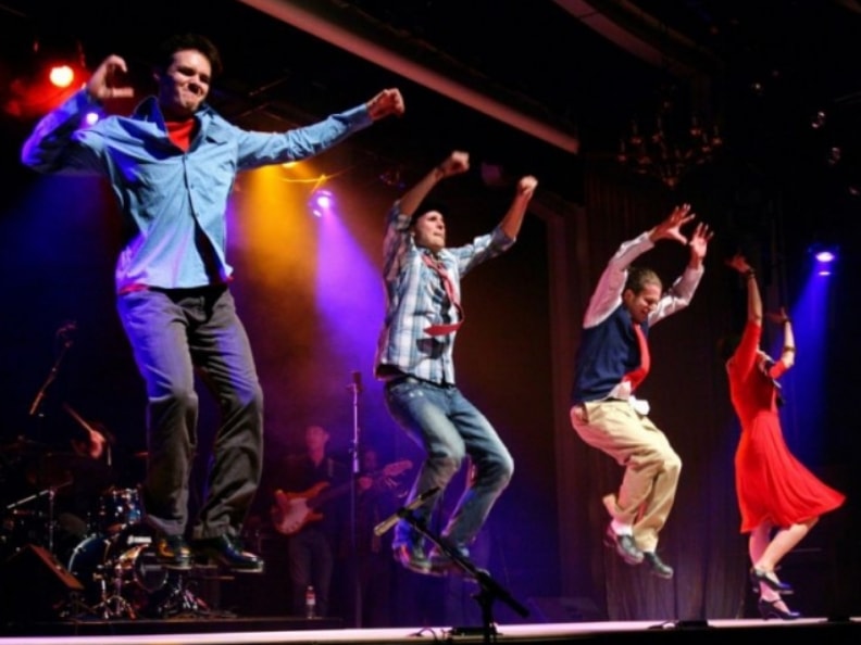 Energetic dance performers jumping on stage with colorful lighting