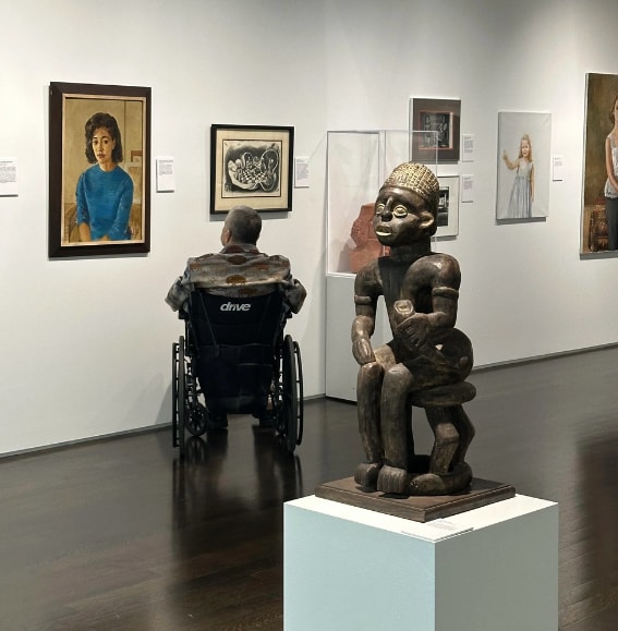 Visitor in wheelchair viewing sculpture and paintings at Pearl Fincher Museum
